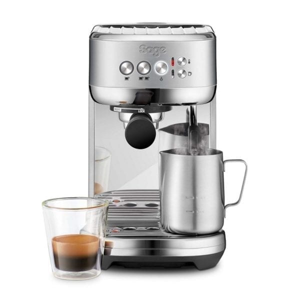 Sage Bambino Plus espresso machine with stainless milk foaming jug and a shot of espresso in a glass.